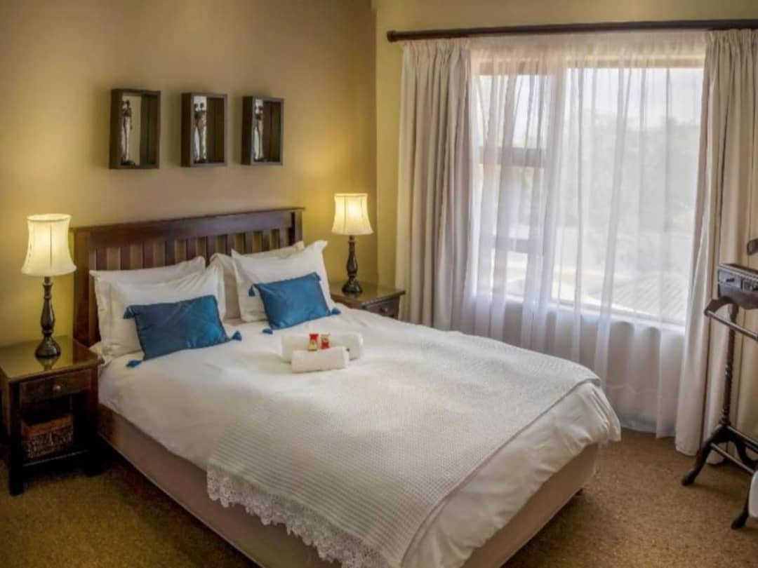 Double bed with teal pillows, bedside lamps, and sheer curtained window.