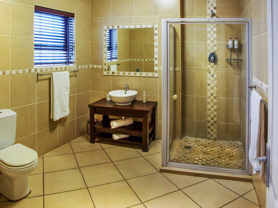 Tiled bathroom with glass shower, vanity basin, toilet and towels.